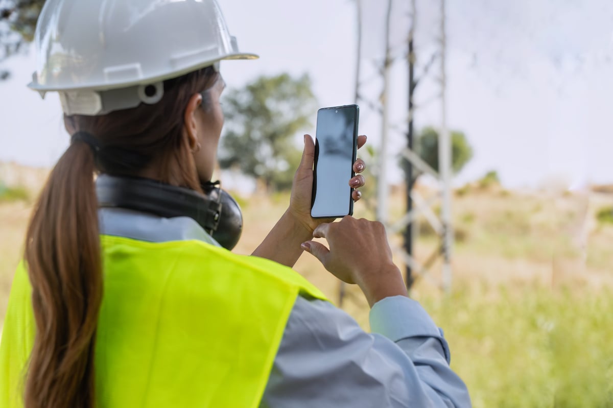 Engineer in hardhat, hi-vis vest, safety glasses, and gloves inspecting a telecommunications tower